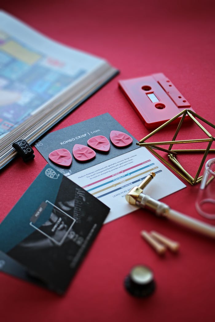 our-journey-01 Artistic display of guitar picks, cassette, and cards on red background.